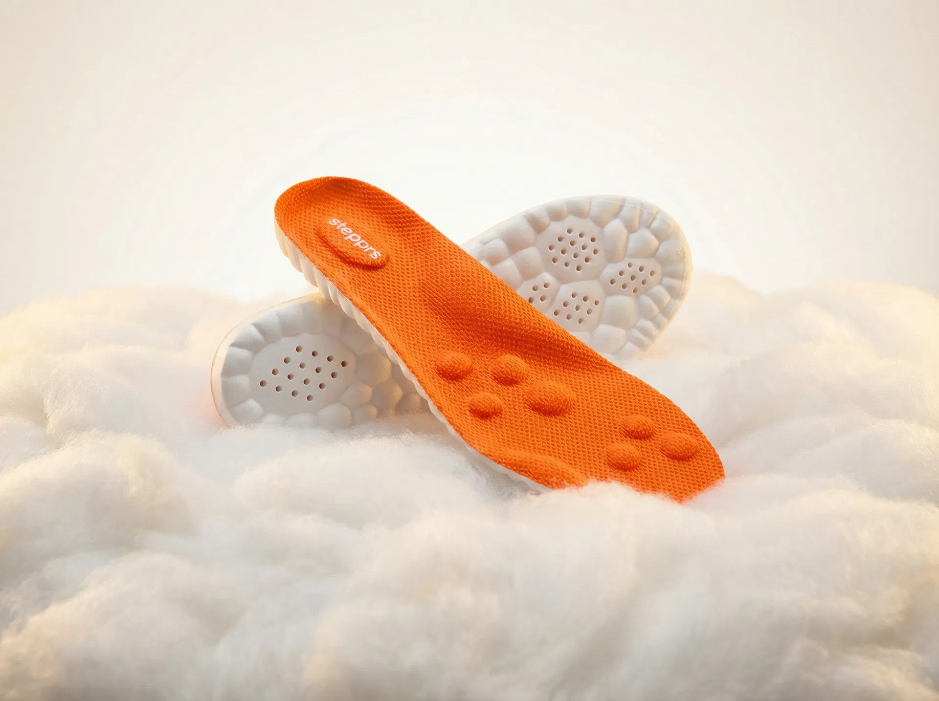 Stepprs orange massage insoles resting on a soft cloud-like surface conveying comfort